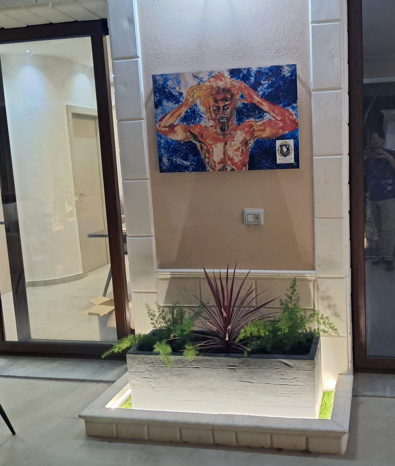Opera d'arte de La Valle Incantata esposta nel patio, con fioriera illuminata di sera