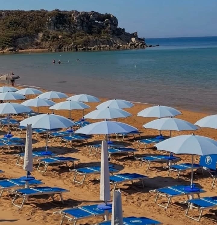 Lido attrezzato con ombrelloni e lettini sulla spiaggia dorata, con la rocca sullo sfondo